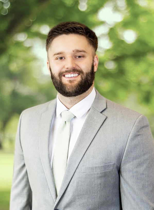 portrait of Trae Pilster, mulat man with dark blonde hair, smiling and wearing light gray blazer, standing outside